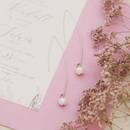 sterling silver artisan pearl earrings on a wedding invitation with floral background