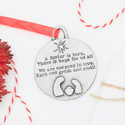 handcrafted babe in a manger pewter ornament set hung on sheer red ribbon stamped with a Christmas story poem on Christmas tree