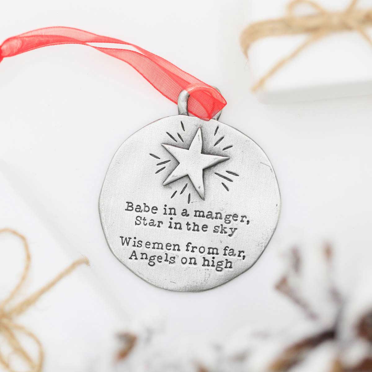 handcrafted babe in a manger pewter ornament set hung on sheer red ribbon stamped with a Christmas story poem on Christmas tree