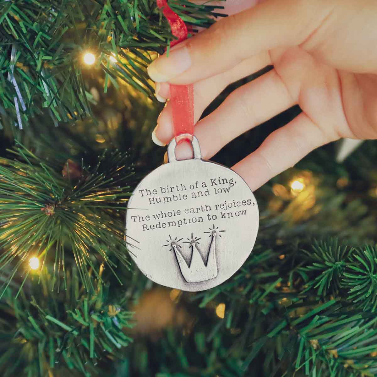 handcrafted babe in a manger pewter ornament set  hung on sheer red ribbon stamped with a Christmas story poem on Christmas tree