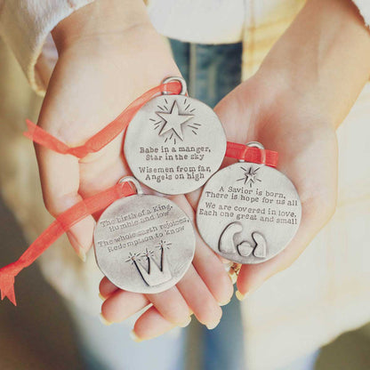 handcrafted babe in a manger pewter ornament set hung on sheer red ribbon stamped with a Christmas story poem on Christmas tree