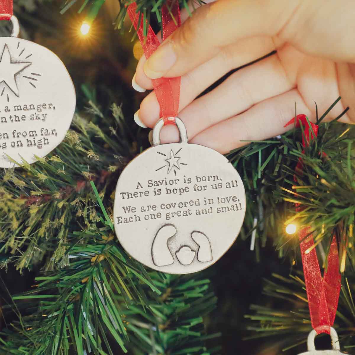 handcrafted babe in a manger pewter ornament set  hung on sheer red ribbon stamped with a Christmas story poem on Christmas tree