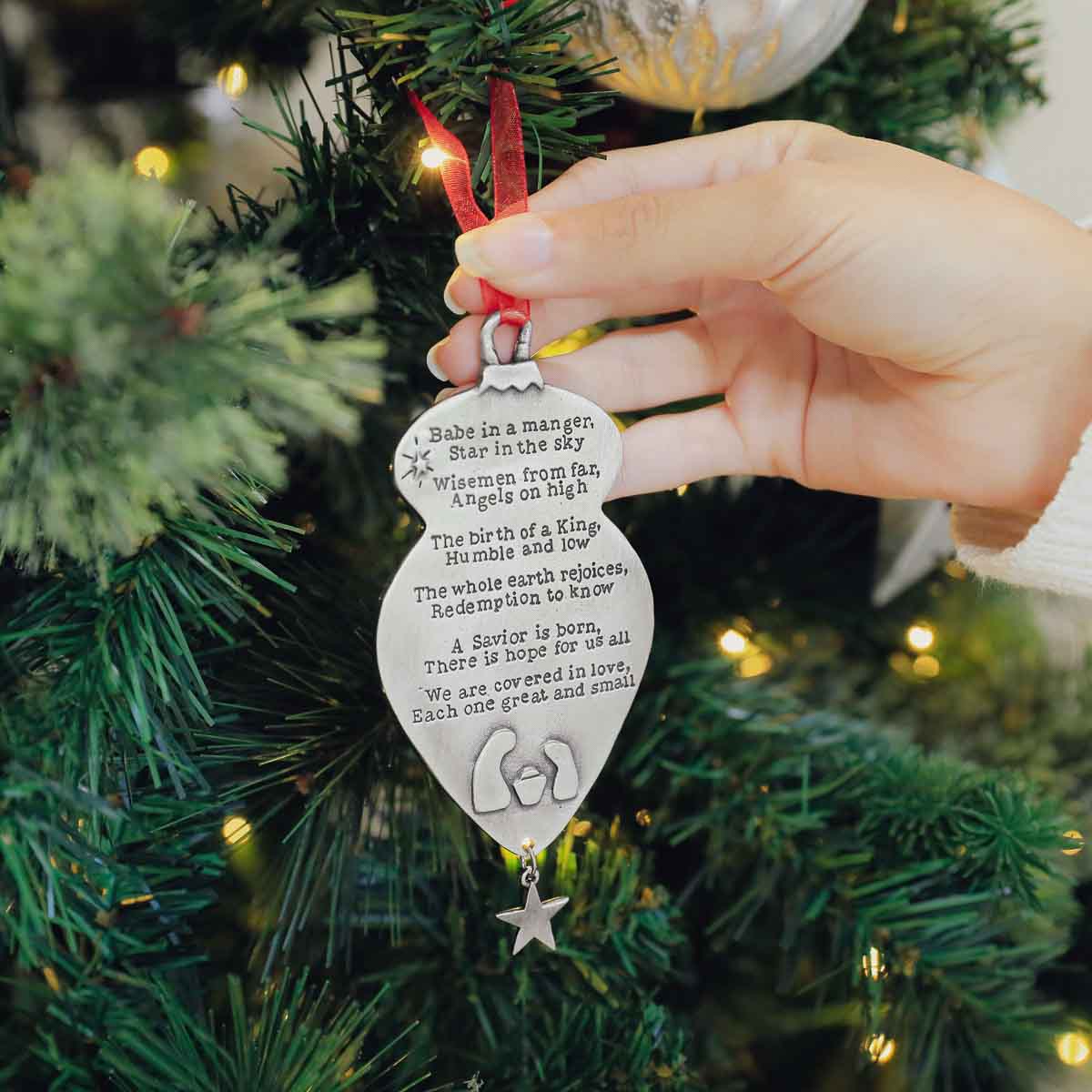 Babe in a manger ornament handcrafted and cast in pewter including a hand-stamped poem being hung on a Christmas tree