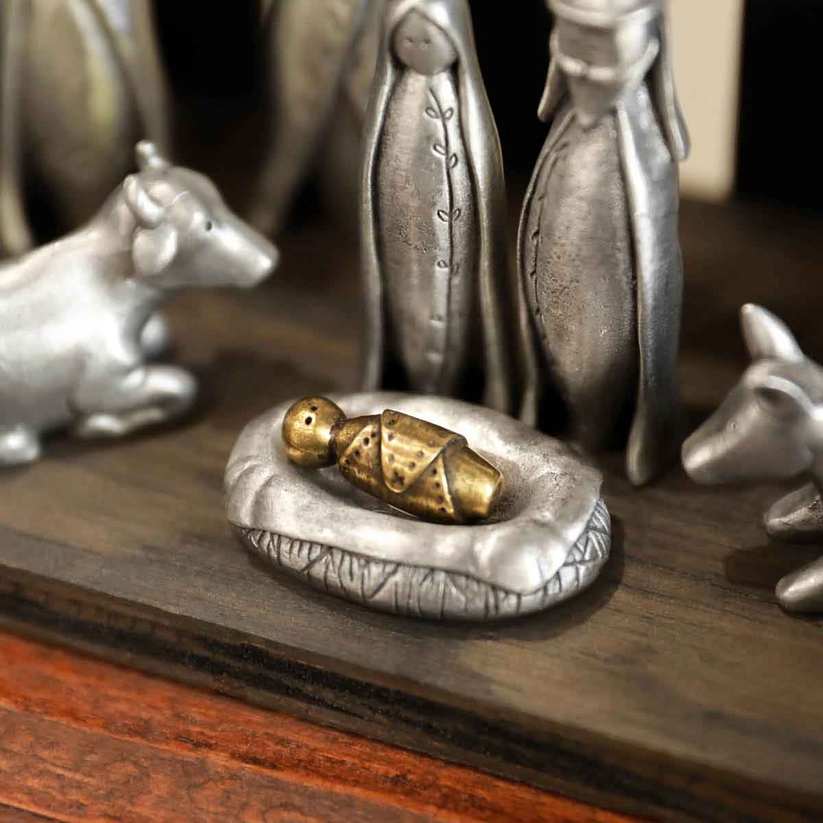 a gold plated baby jesus nativity figurine in a pewter manger