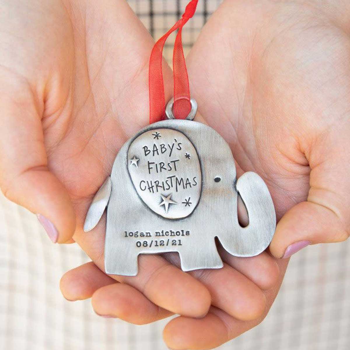 hand holding a baby's first Christmas ornament of an elephant hand-molded and cast in fine pewter. personalized with up to two lines with a name, phrase or date being 