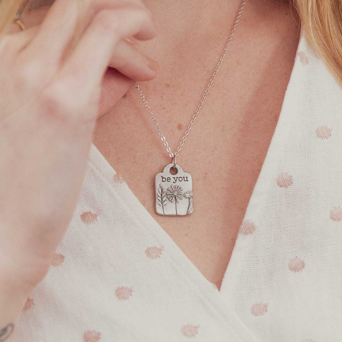 Girl wearing her Be you necklace handcrafted in pewter hung on a silver-toned link chain with the words "be you" engraved