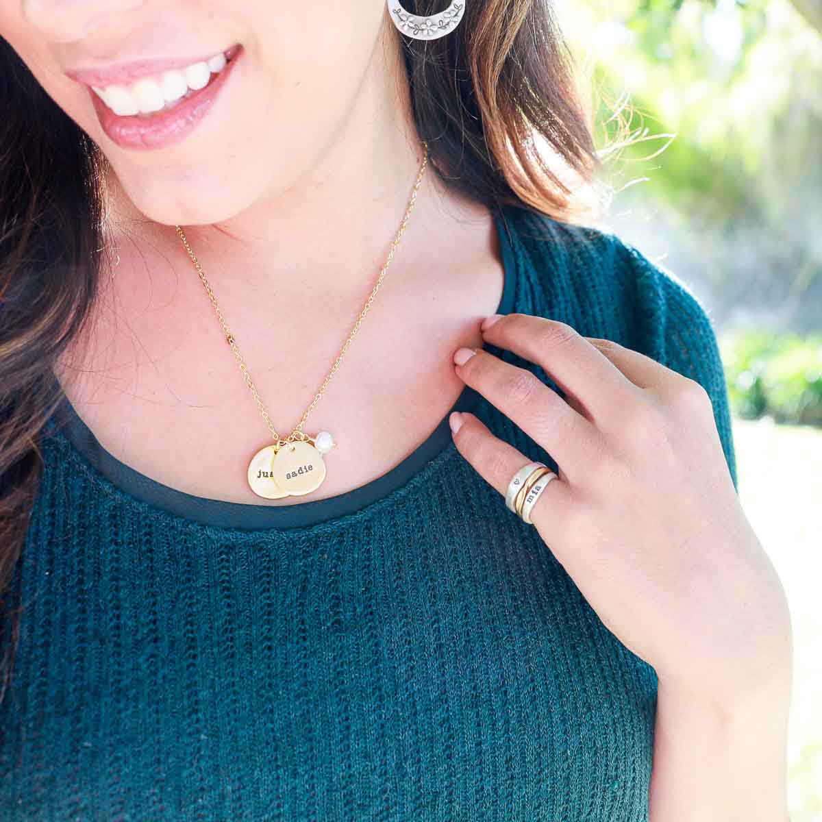 Girl wearing her Beloved name disc handcrafted in 10k yellow gold hung with a vintage freshwater pearl and customizable with a name or word along with other sterling silver jewelry