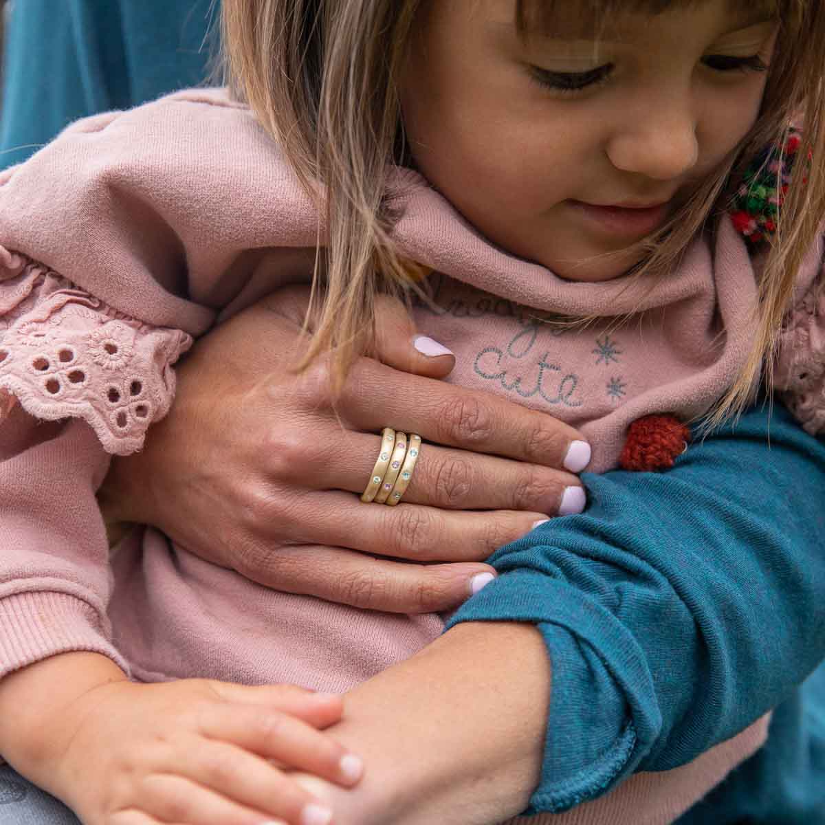 Girl wearing her Stackable birthstone rings handcrafted in 10k yellow gold with 2mm birthstones holding her daughter 