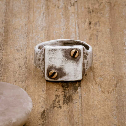 the Bonded Rivet Ring, handcrafted in sterling silver with bronze rivets and a textured finish, on a wood background