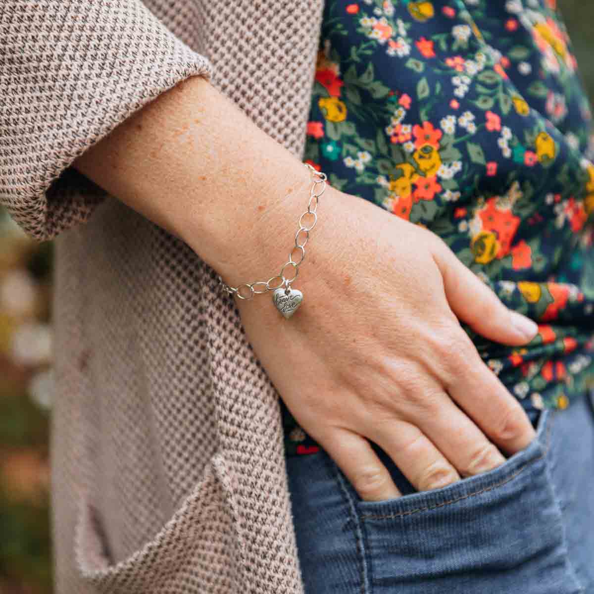 Woman wearing her handcrafted sterling silver Brave Love emblem bracelet with a matte brushed finish