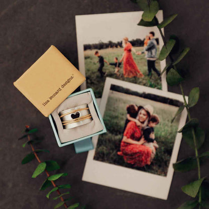 close up of brave love® spinner ring {sterling silver & 10k gold} in a ring box with family photos