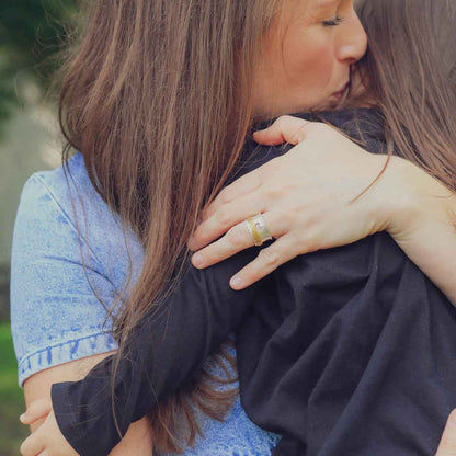 mom wearing brave love spinner ring {sterling silver & 10k gold} holding and kissing daughter