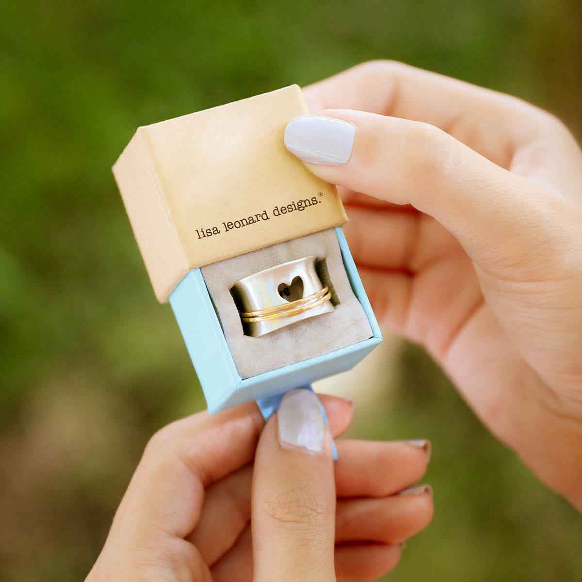 close up of girl holding brave love® spinner ring {sterling silver & 10k gold} in a ring box