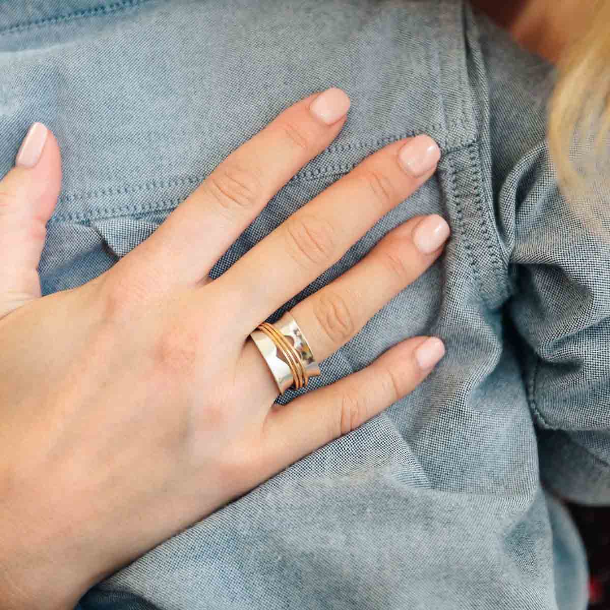 Woman wearing Brave Love spinner ring with a sterling silver band and gold-filled spinners and engraved with "brave love" on the inside