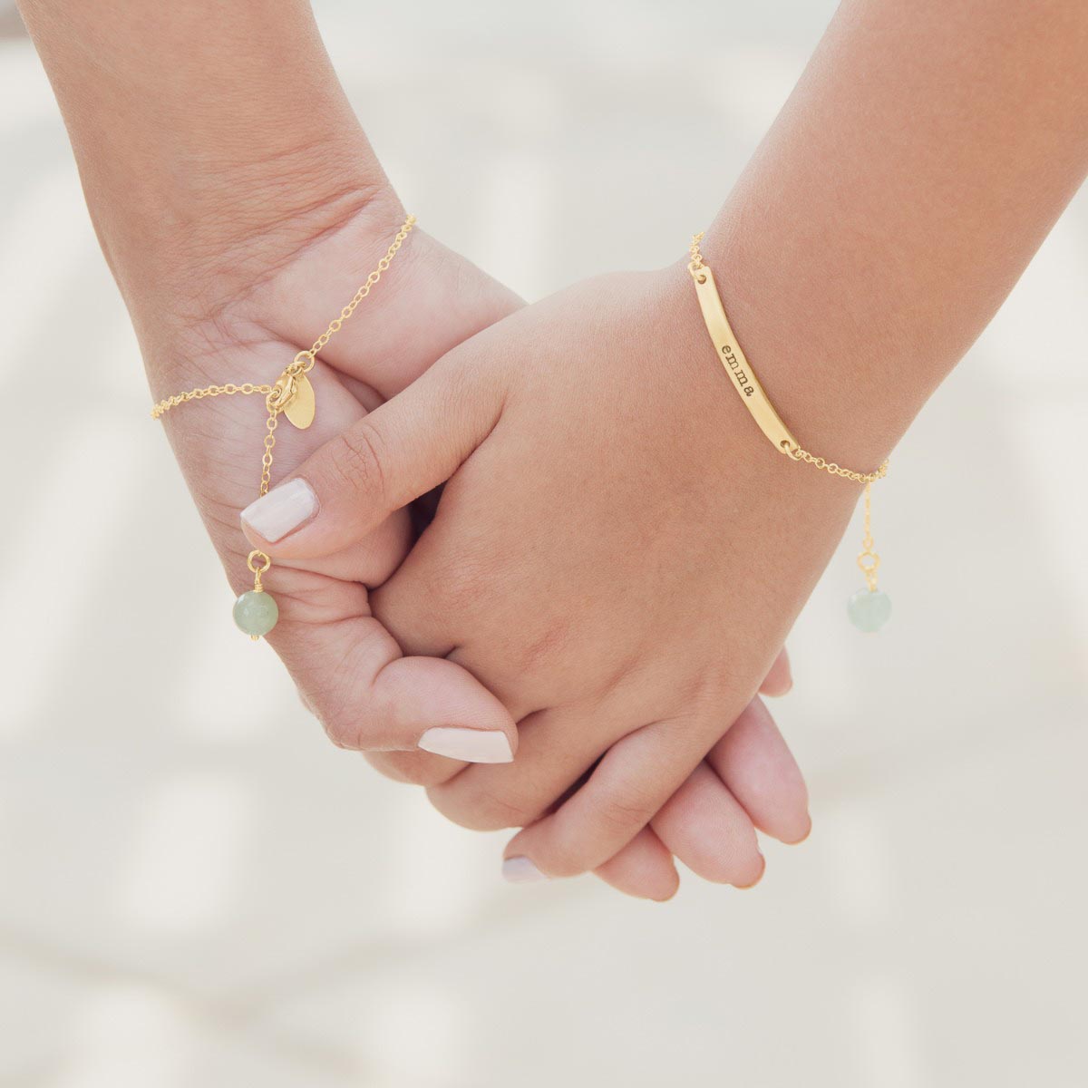 Friends holding hands wearing their personalized carry my heart 10k yellow gold bracelet with aventurine stone