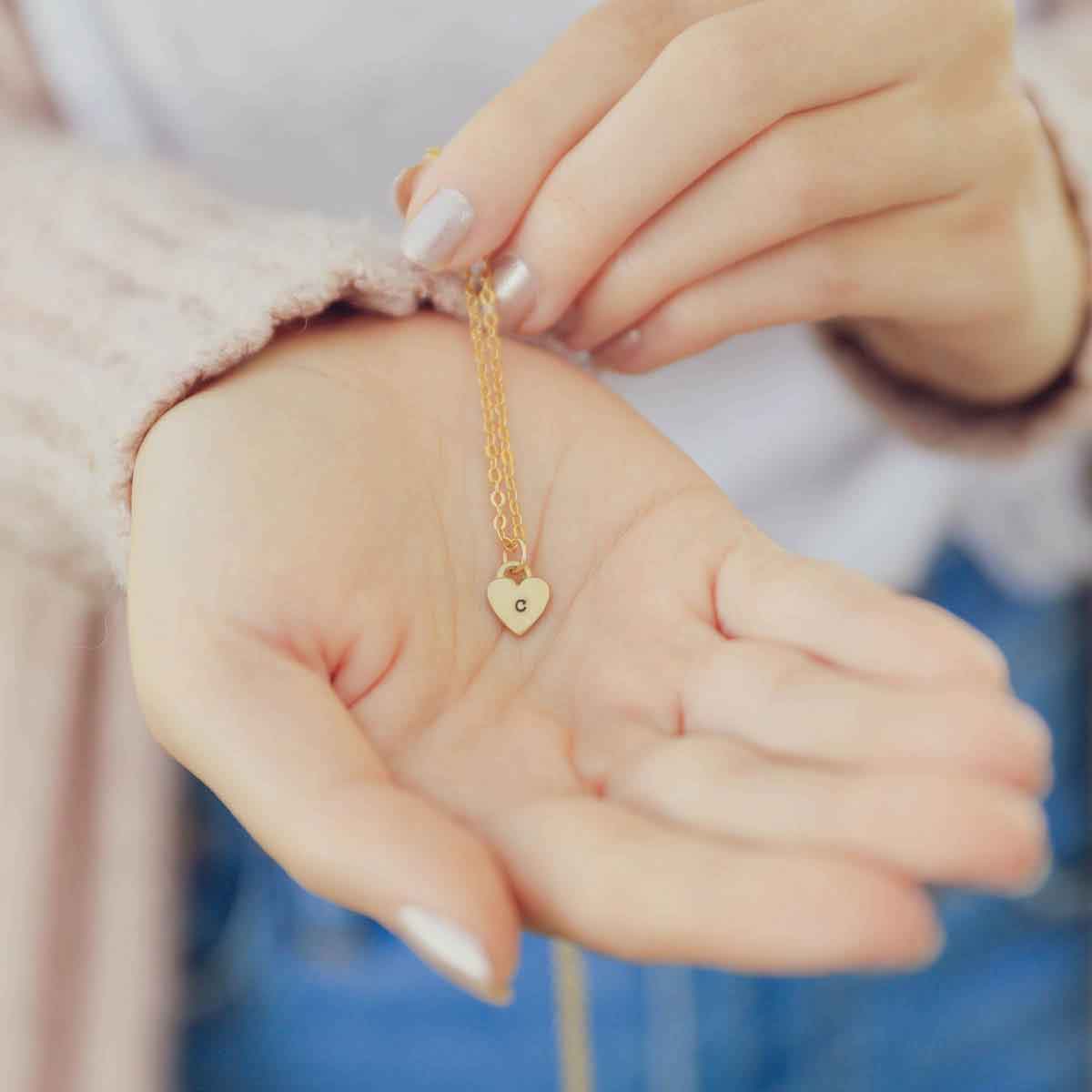 Woman holding her Cherished hearts initials necklace handcrafted in 10k yellow gold with personalized charms