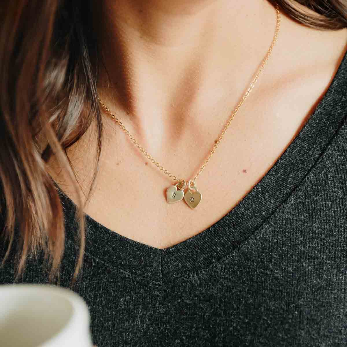 Woman wearing her Cherished hearts initials necklace handcrafted in 10k yellow gold including two customizable charms