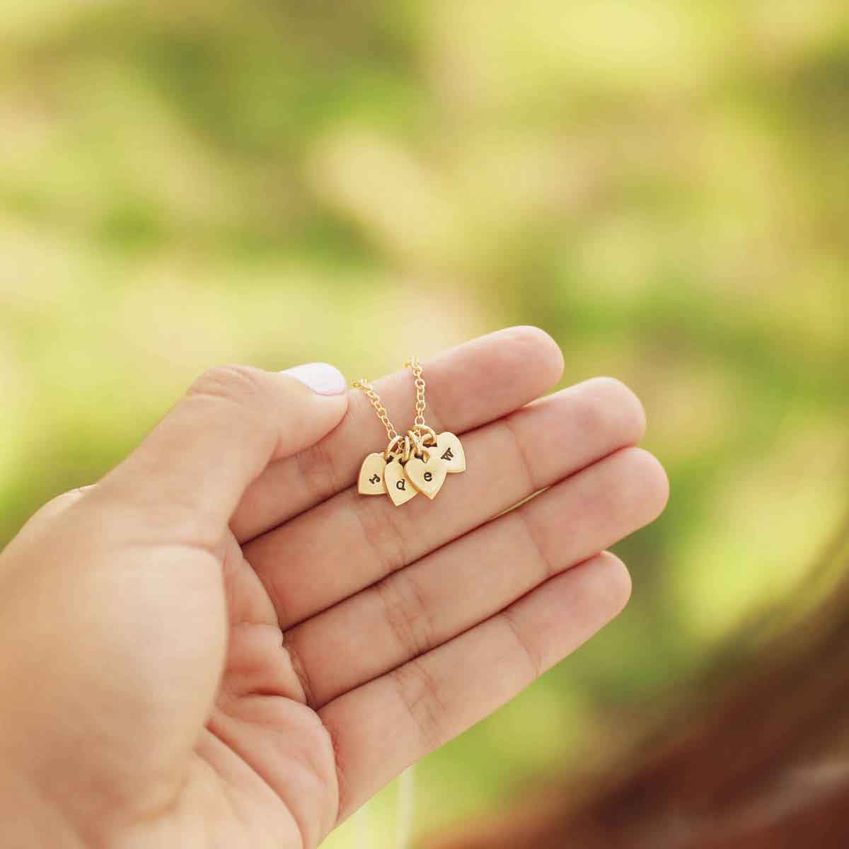 Woman holding her Cherished hearts initials necklace handcrafted in 14k yellow gold including customizable charms