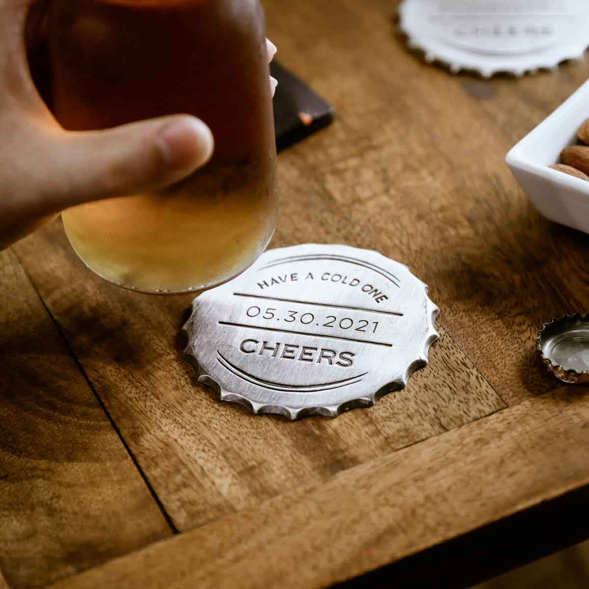 close up of the Crafting Memories Coaster on a wooden table with a hand holding a beer bottle 