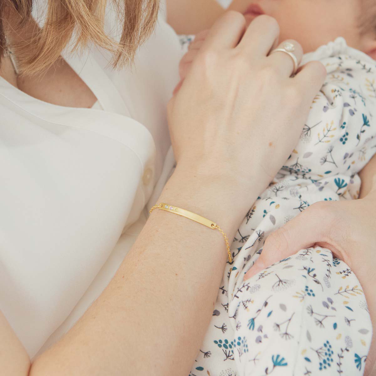 Woman holding her baby wearing her handcrafted 14k cross bar birthstone bracelet