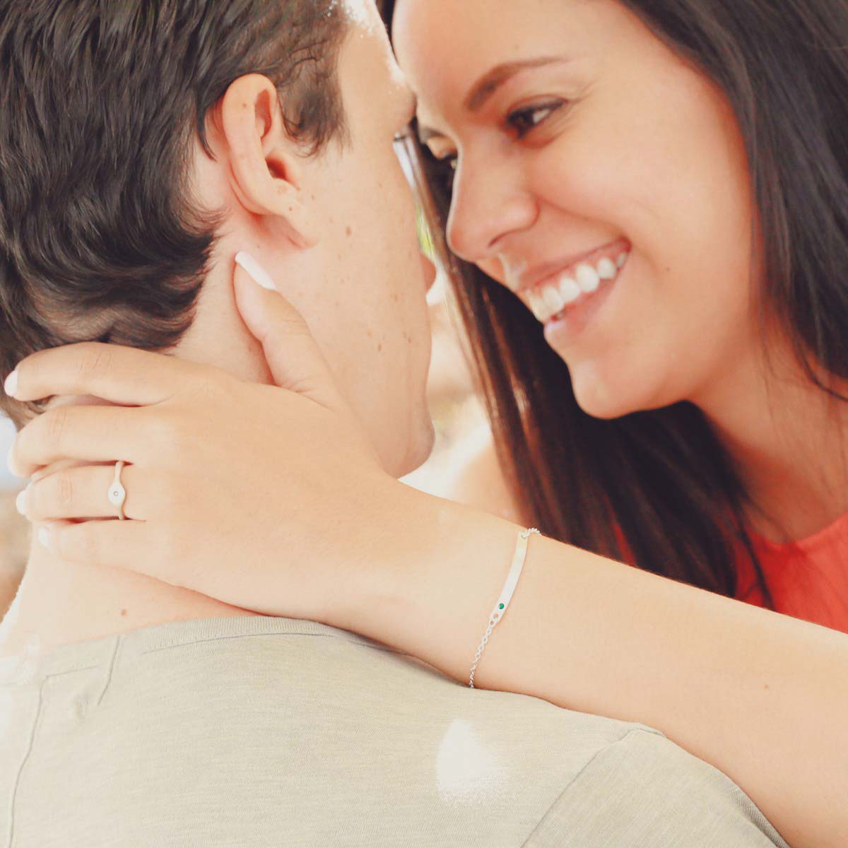 A couple embracing with woman showing her sterling silver jewelry including a cross bar birthstone bracelet