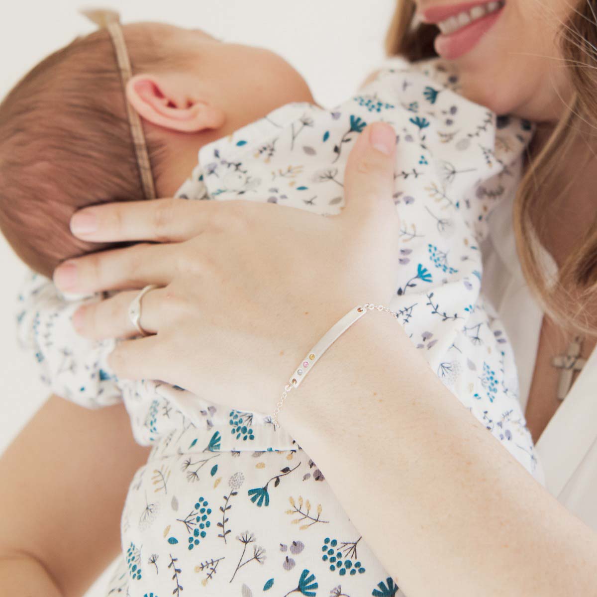 Woman holding her baby while wearing her personalized sterling silver cross bar birthstone bracelet