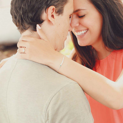 A couple embracing with woman showing her sterling silver jewelry including a cross bar birthstone bracelet