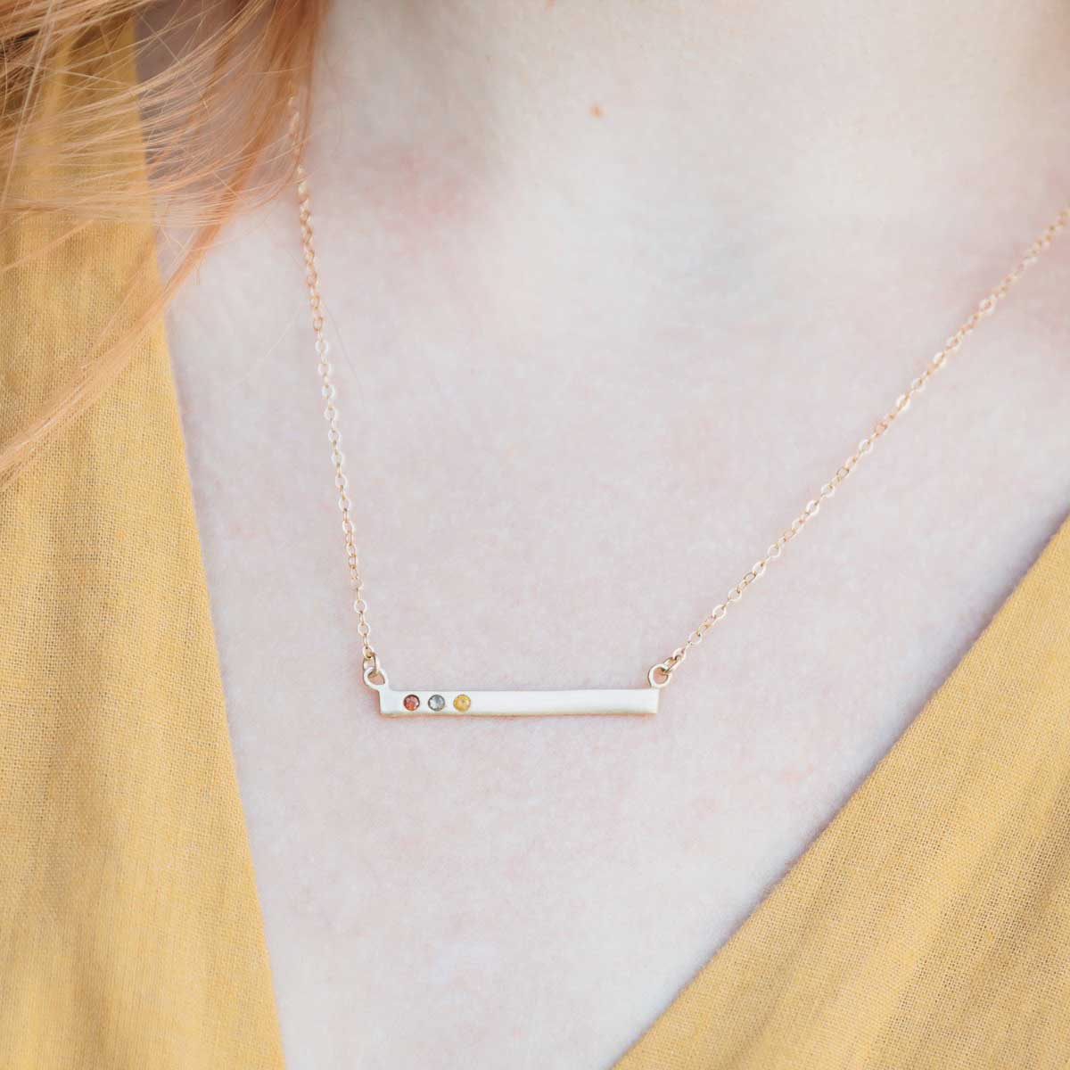 girl wearing 10k yellow gold cross bar birthstone necklace strung on a gold-filled link chain customizable with up to 7 genuine 2mm birthstones 