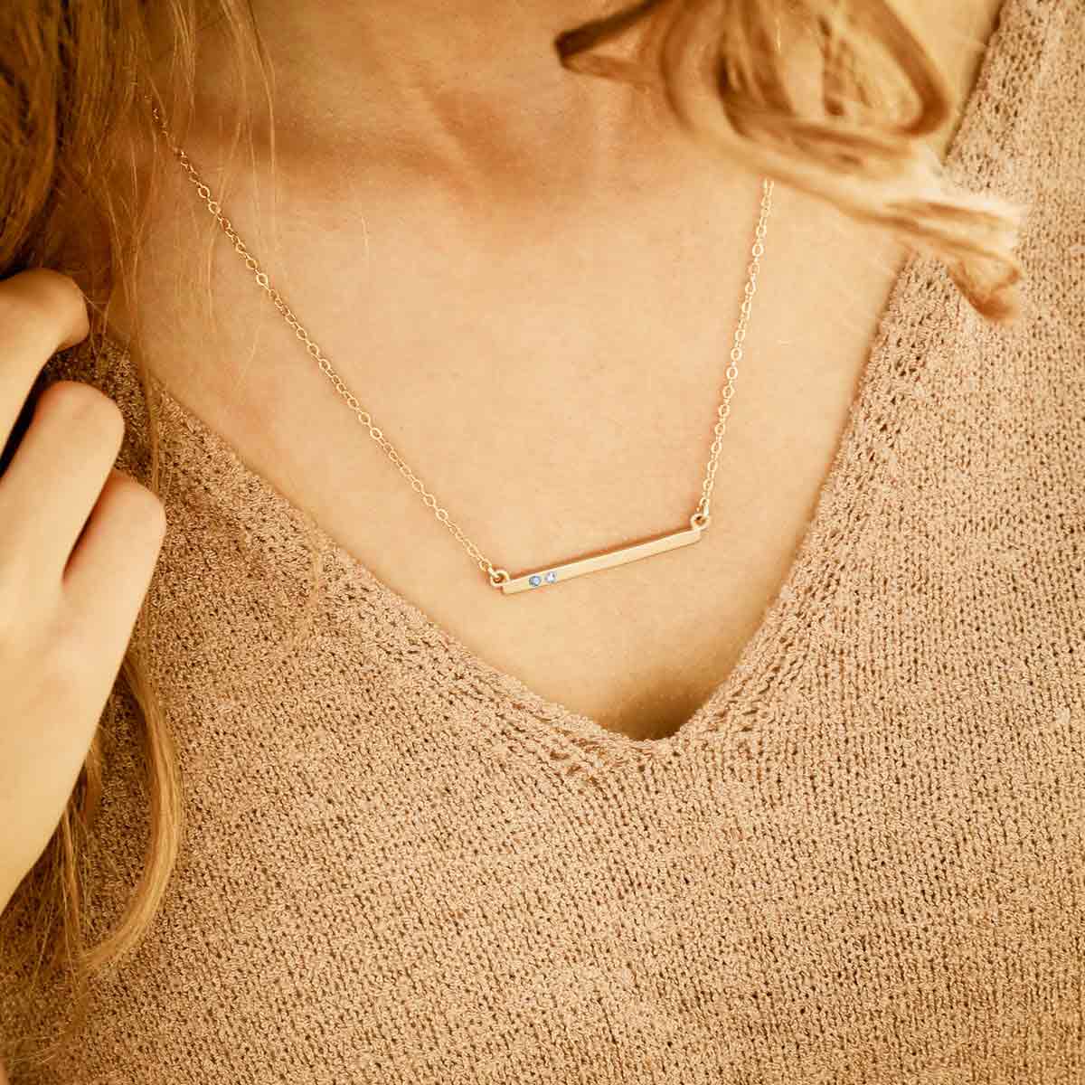 girl wearing 14k yellow gold cross bar birthstone necklace strung on a gold-filled link chain customizable with up to 7 genuine 2mm birthstones 