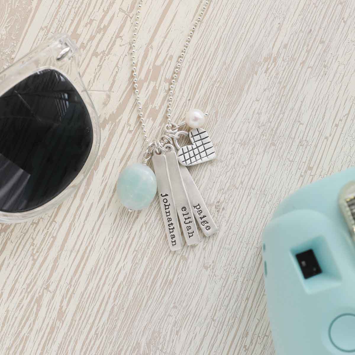 Cross my heart necklace handcrafted in sterling silver with silver tags personalized with a special name hung next to a vintage freshwater pearl and an aqua stone