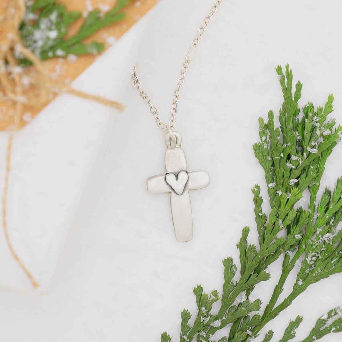 sterling silver cross of faith necklace on white snow and some greenery