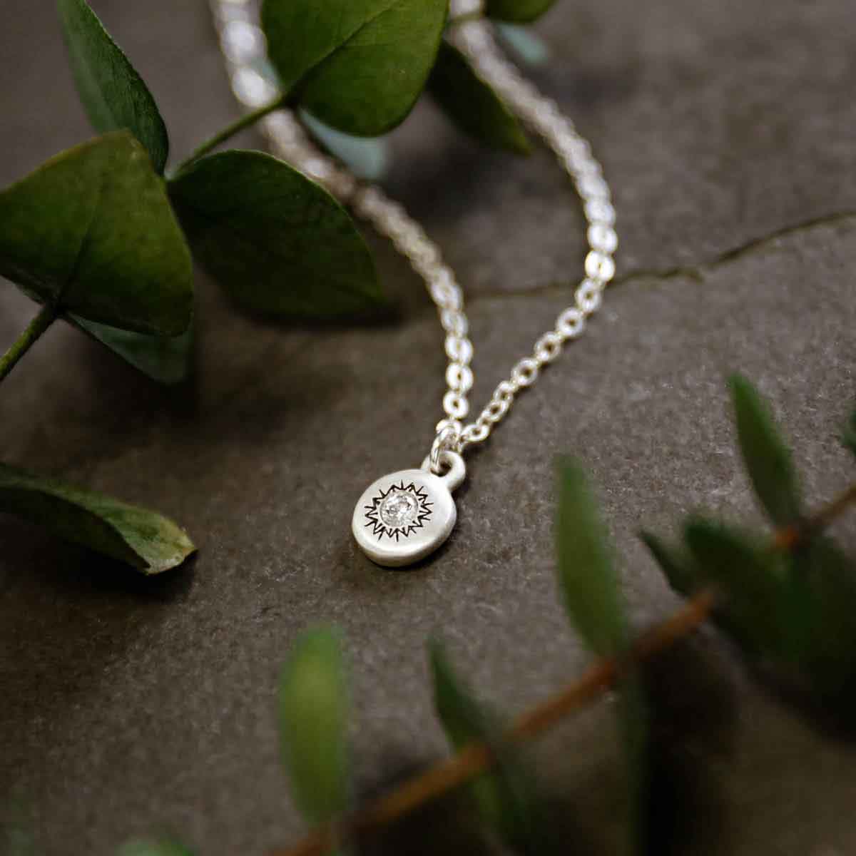 girl holding a Dainty Sunburst Necklace cast in Sterling Silver and set with a 3mm cubic zirconia stone