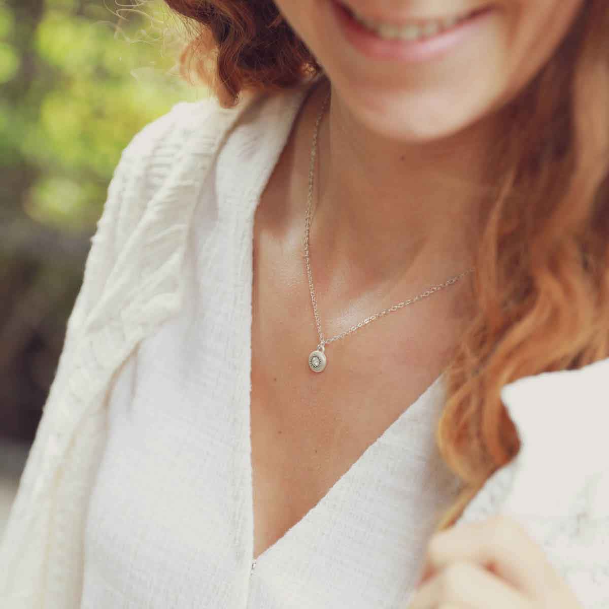 girl holding a Dainty Sunburst Necklace cast in Sterling Silver and set with a 3mm cubic zirconia stone