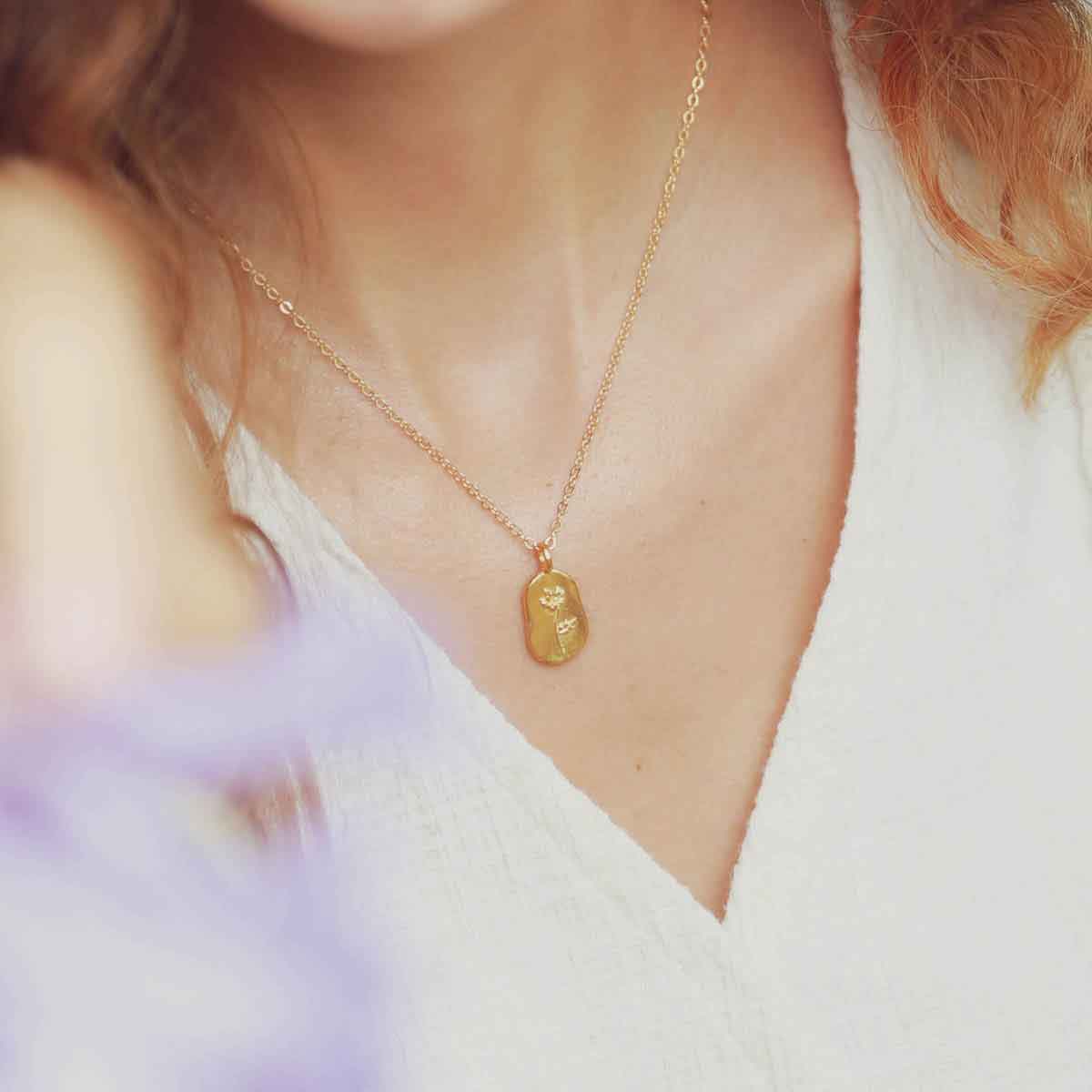 girl holding a gold plated February birth flower necklace with an 18" gold filled link chain