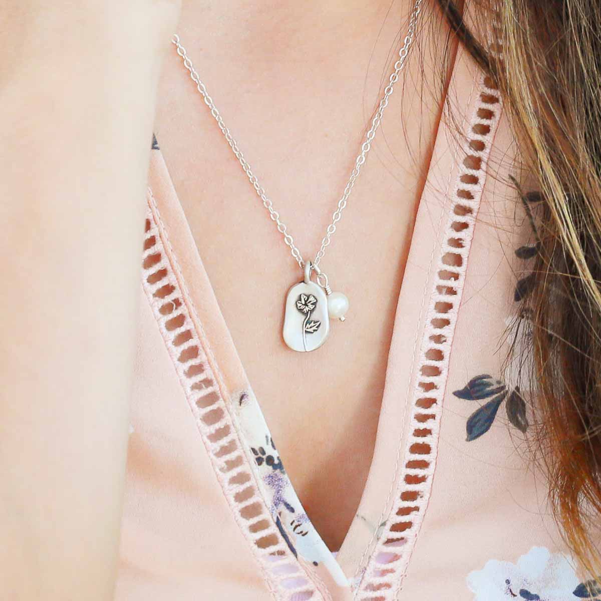 Girl wearing her February birth flower necklace handcrafted in sterling silver with a special birth month charm strung with a vintage freshwater pearl