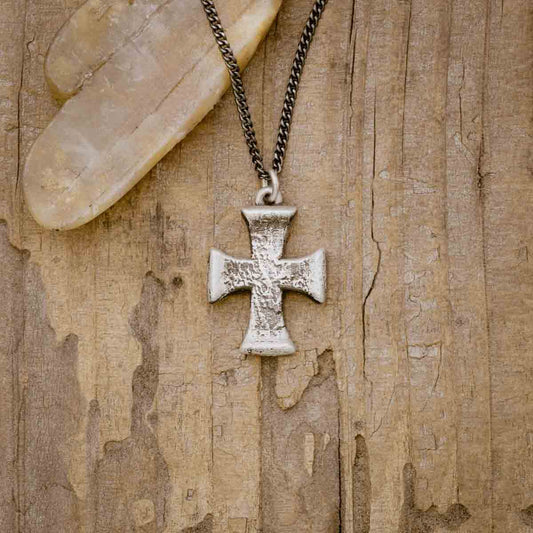 a sterling silver Flourish Cross Necklace on a wood background