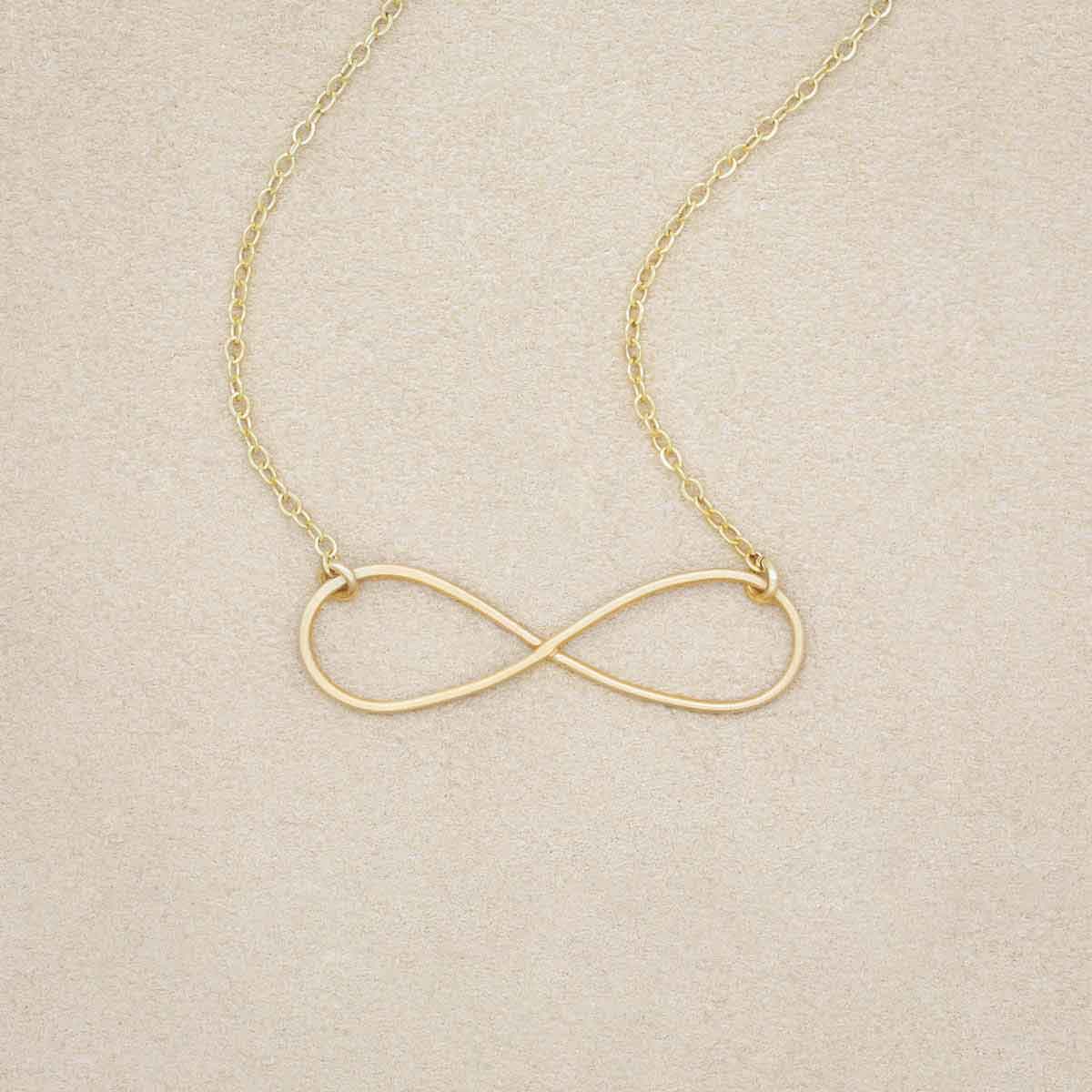 A gold filled Forever, For Always Infinity Necklace, on a beige background