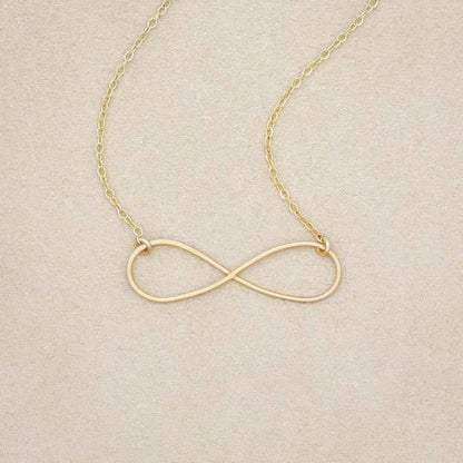 A gold filled Forever, For Always Infinity Necklace, on a beige background