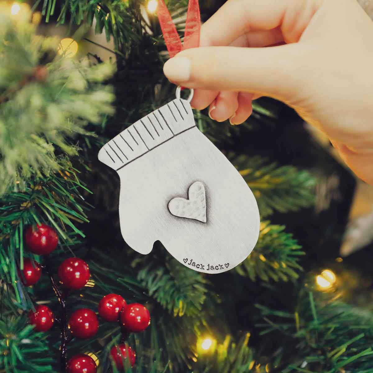 hand hanging a pewter found mitten ornament on a christmas tree