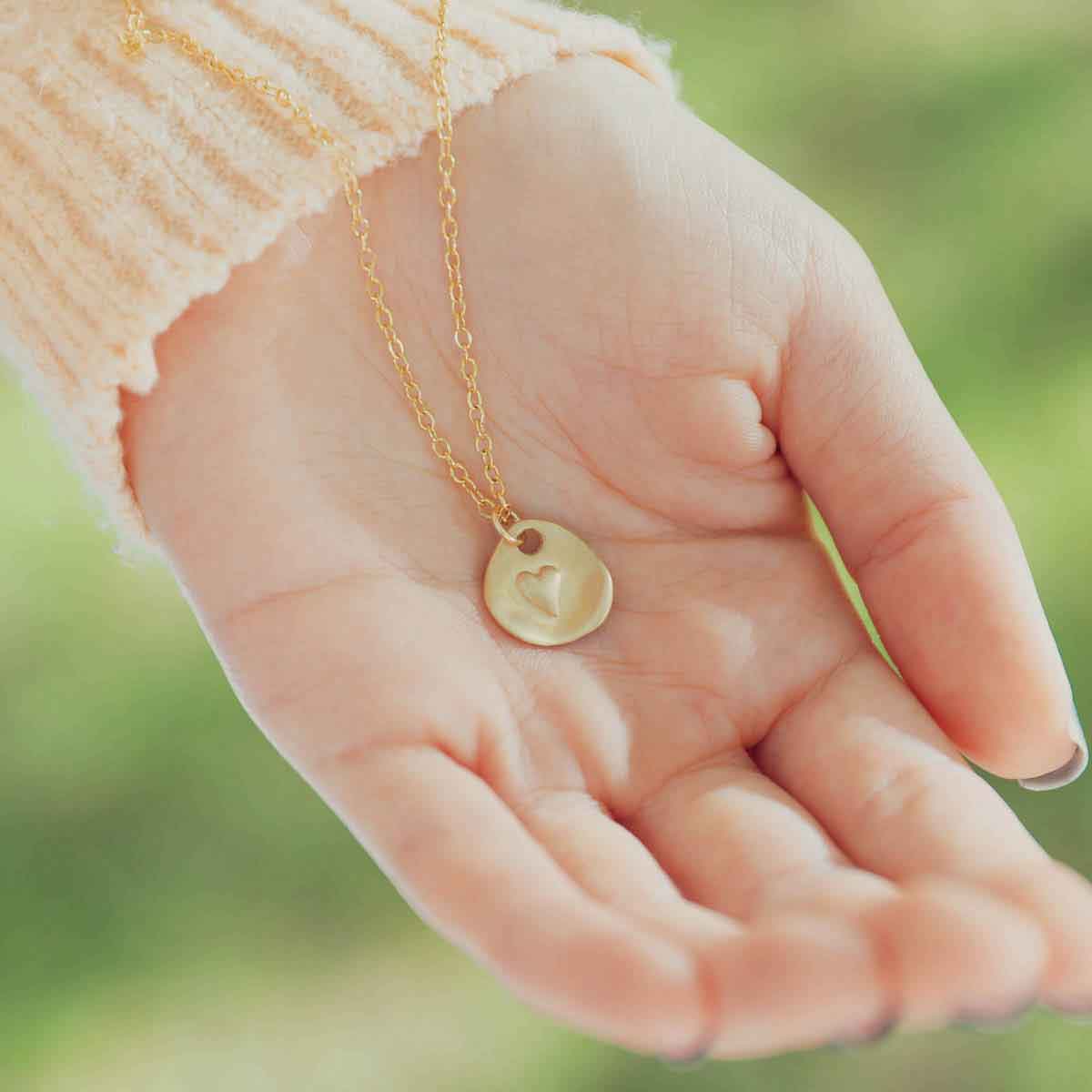 girl's hand holding 14k yellow gold full of love necklace strung on gold-filled link chain