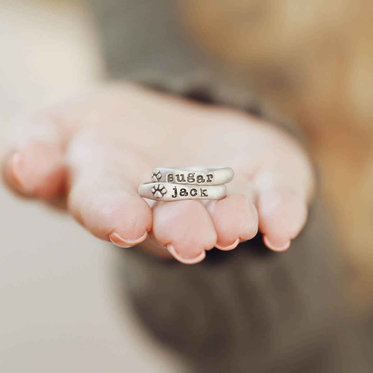 Woman holding her furry footprint sterling silver stacking rings personalized with her pet names