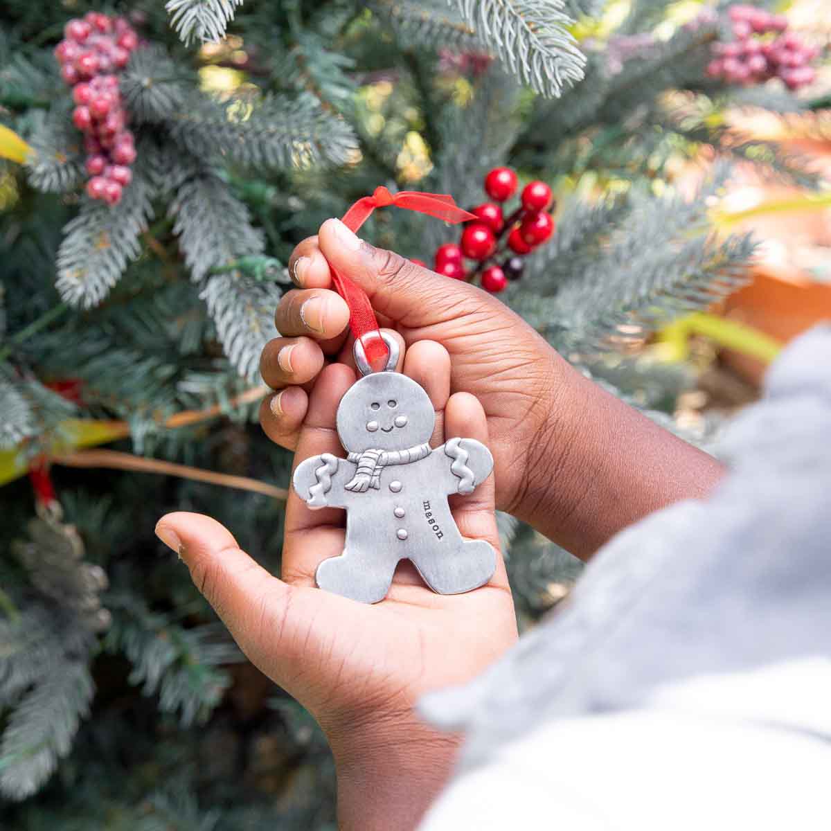 Gingerbread boy ornament  hand-molded and cast in fine pewter hung from a sheer red ribbon with a personalized word being placed on Christmas tree