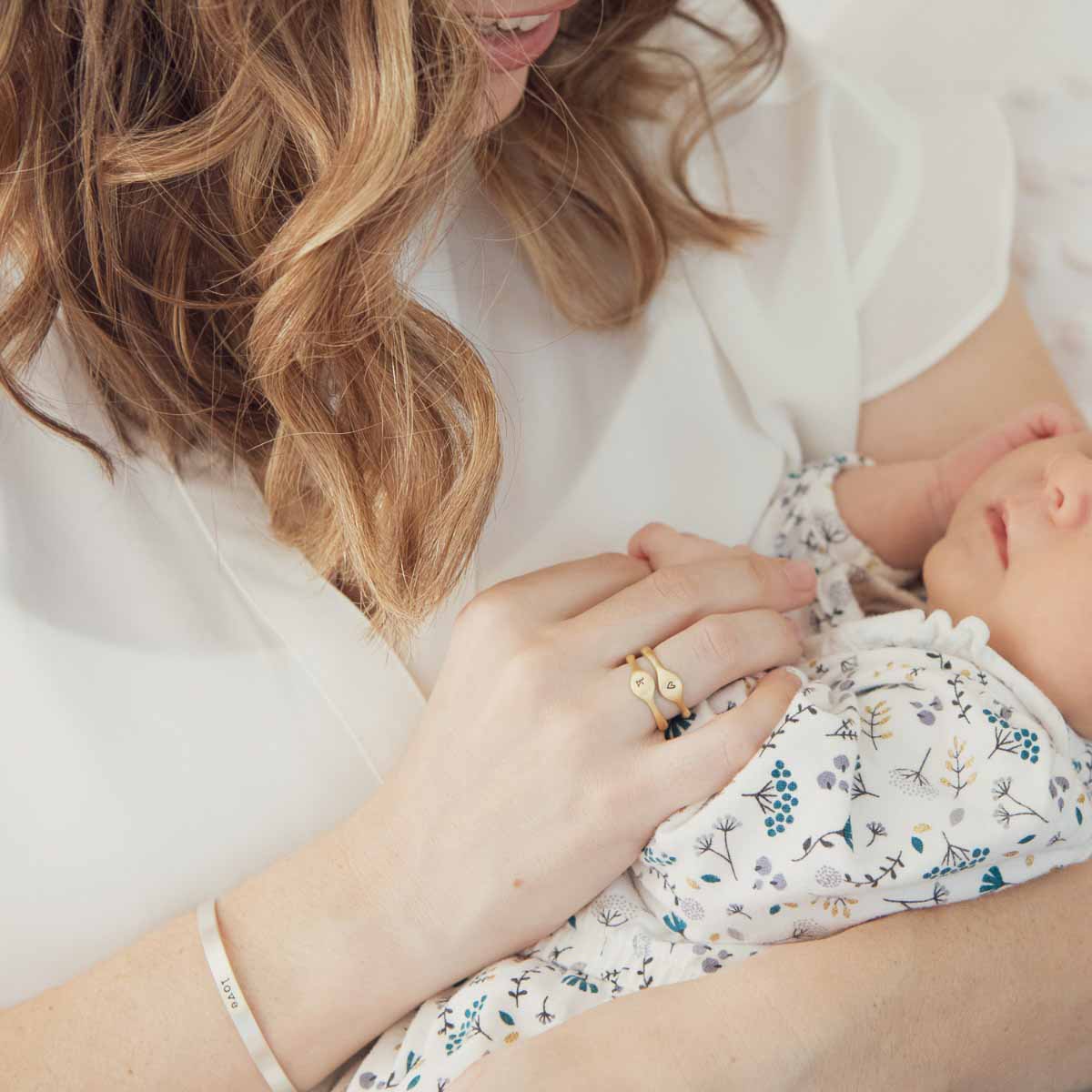 Mom wearing her Initial stacking ring handcrafted and cast in 10k yellow gold then hand-stamped with an initial holding her baby