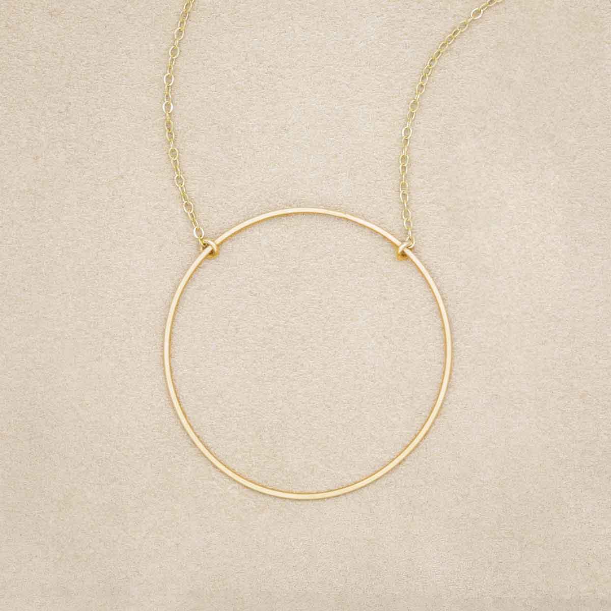 A gold filled It All Matters Circle Necklace, on beige background
