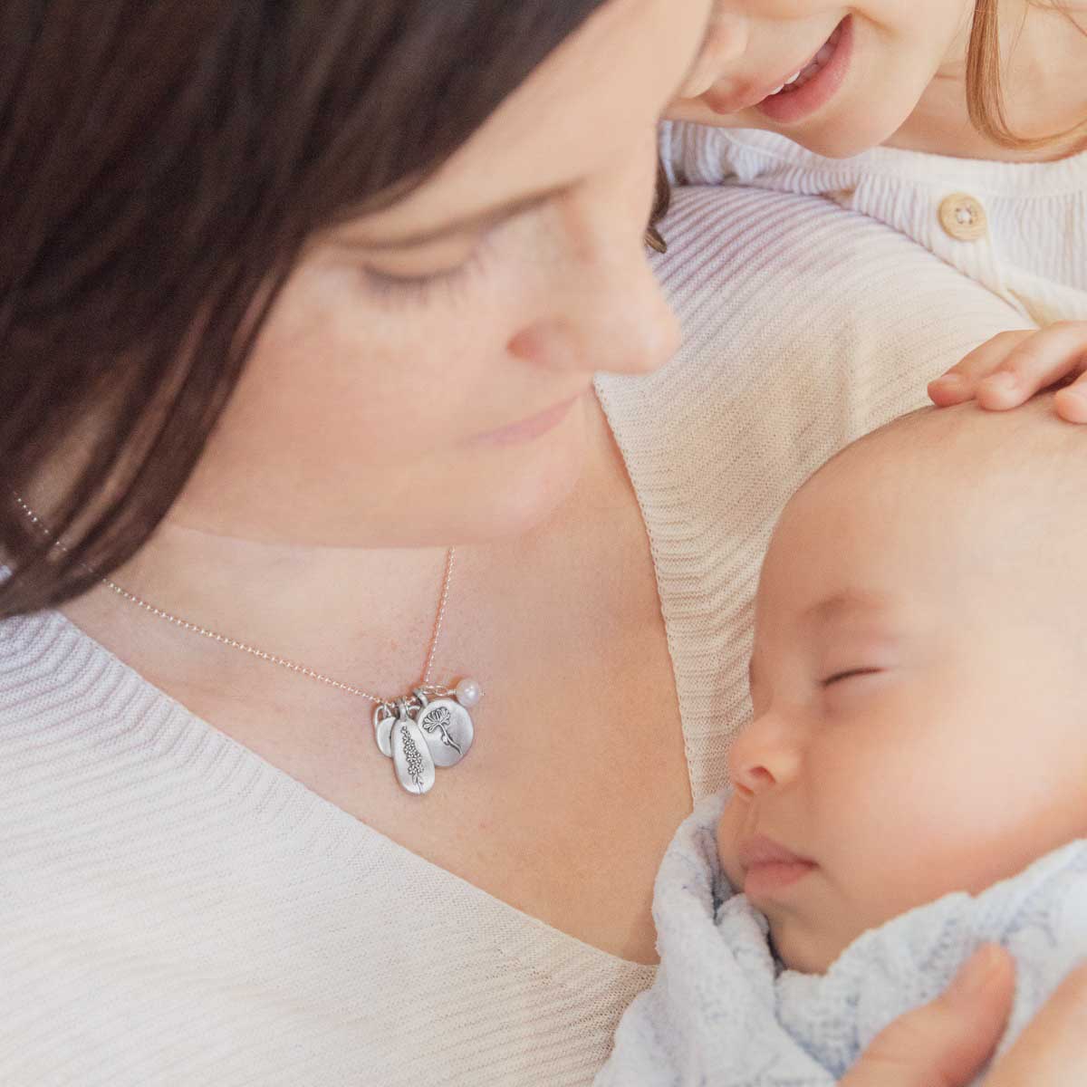 Girl wearing her July birth flower necklace handcrafted in sterling silver with a special birth month charm strung with a vintage freshwater pearl with her baby