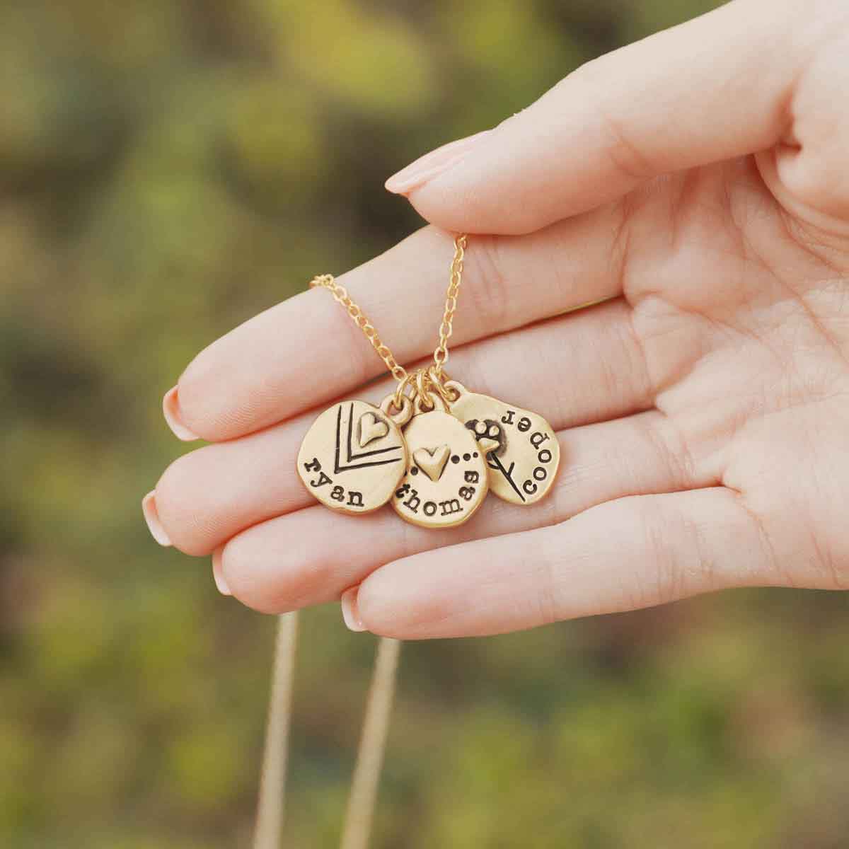 woman holding her handcrafted 14k yellow gold personalized jumble of love necklace with a gold charm