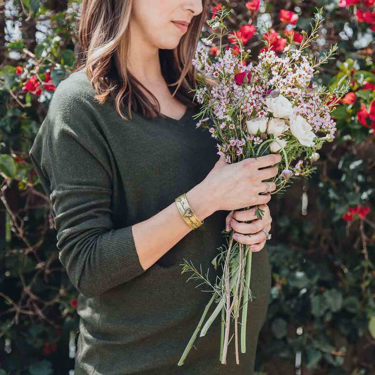 Woman holding flowers while wearing her bronze let love grow cuff bracelet