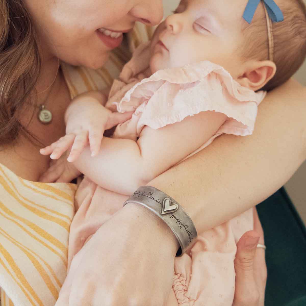 mother holding baby wearing pewter let love grow cuff