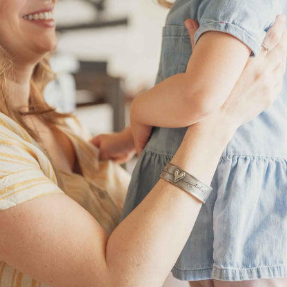 mother wearing pewter let love grow cuff holding baby girl