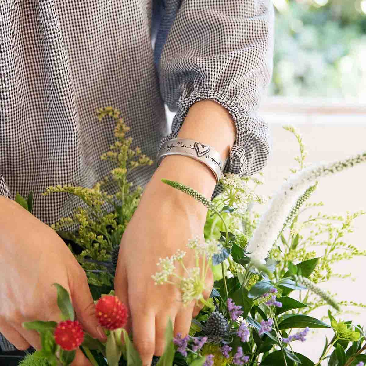 Girl showing her handcrafted pewter let love grow cuff next to flowers